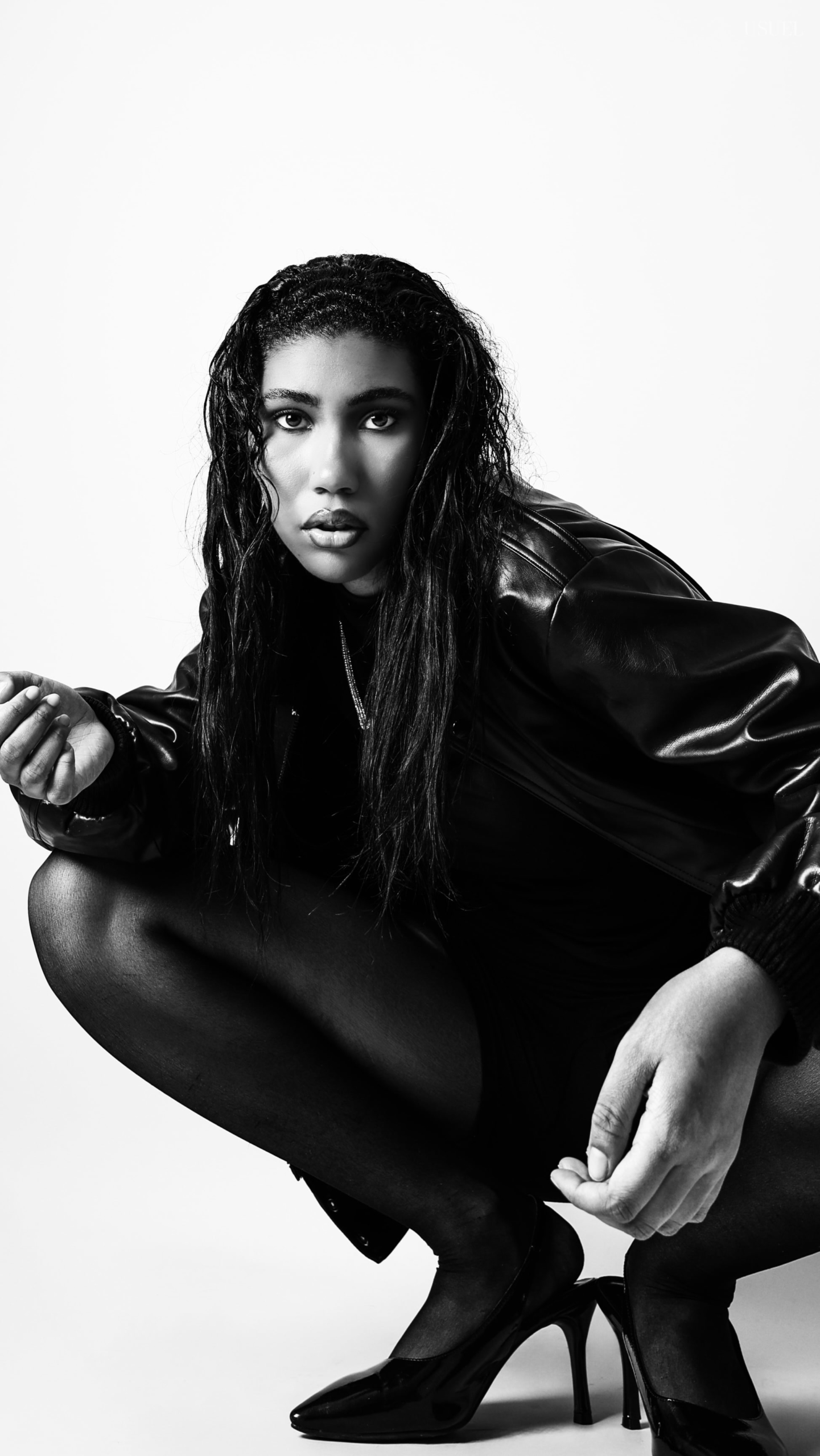 Black and white photo of a woman on a white background, wearing a bold black leather jacket and delicate tights, with an elegant silhouette and confident posture