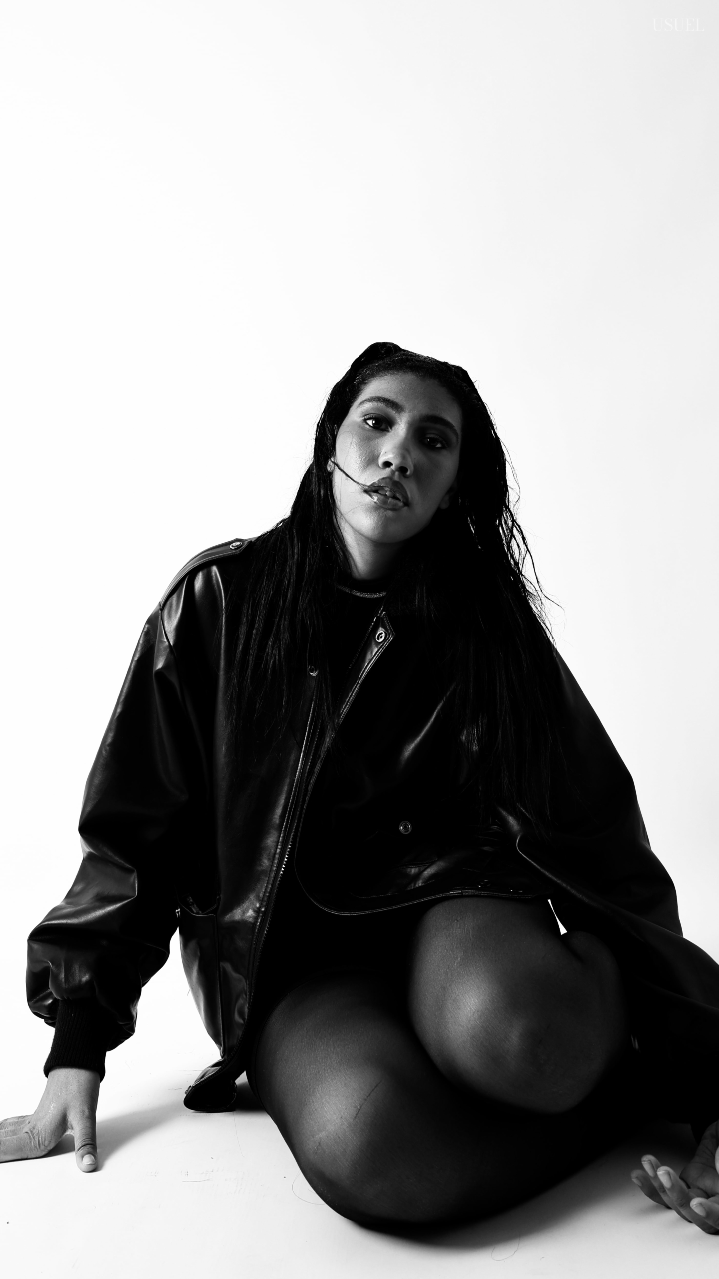 Black and white photo of a woman on a white background, wearing a bold black leather jacket and delicate tights, with an elegant silhouette and confident posture