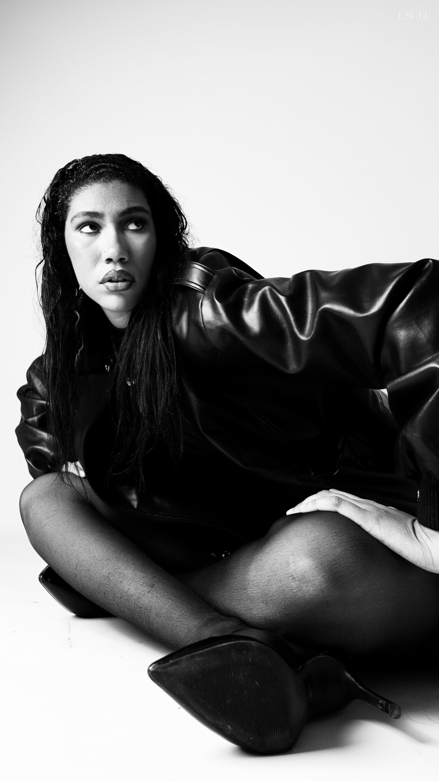 Black and white photo of a woman on a white background, wearing a bold black leather jacket and delicate tights, with an elegant silhouette and confident posture