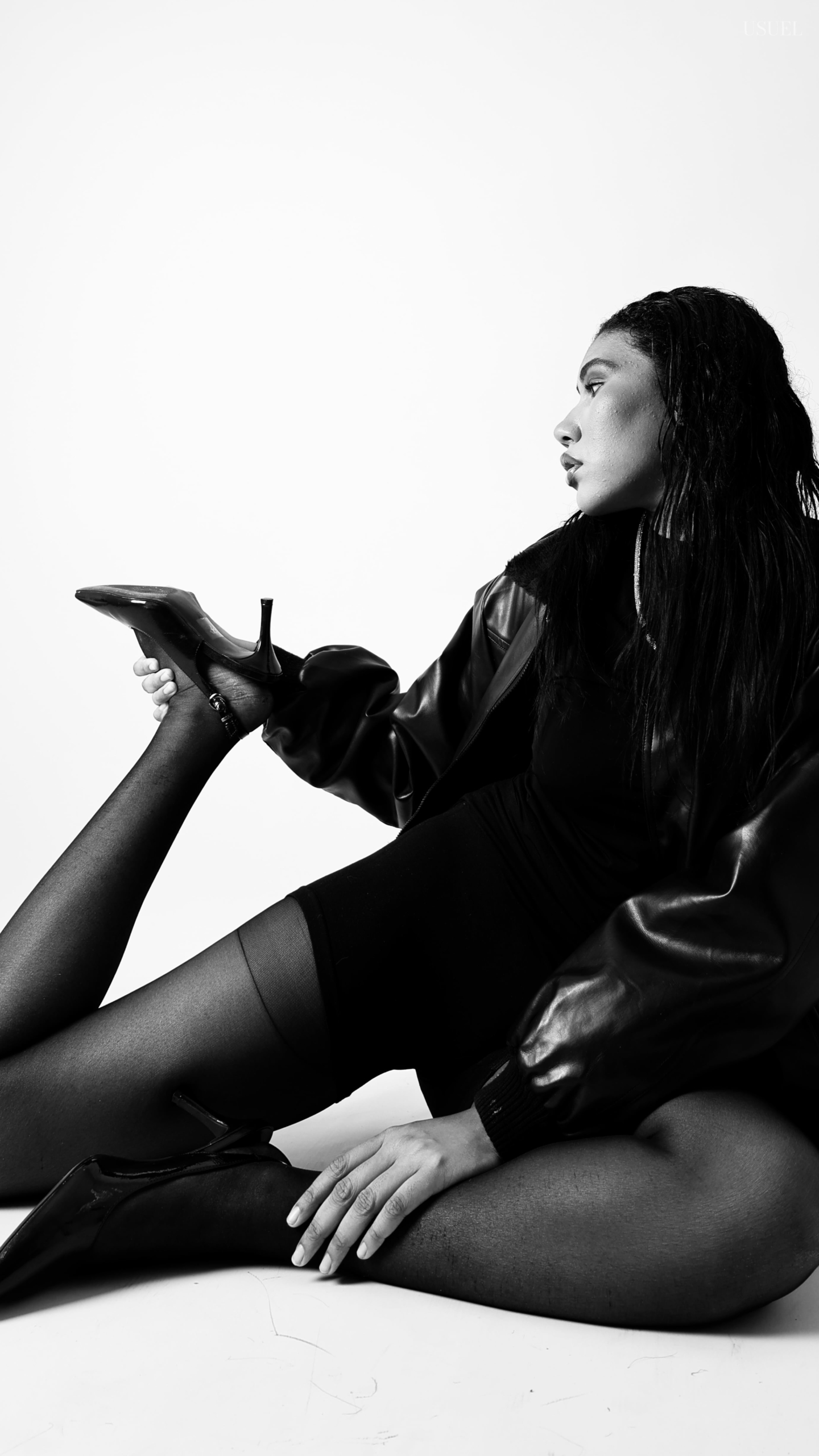 Black and white photo of a woman on a white background, wearing a bold black leather jacket and delicate tights, with an elegant silhouette and confident posture