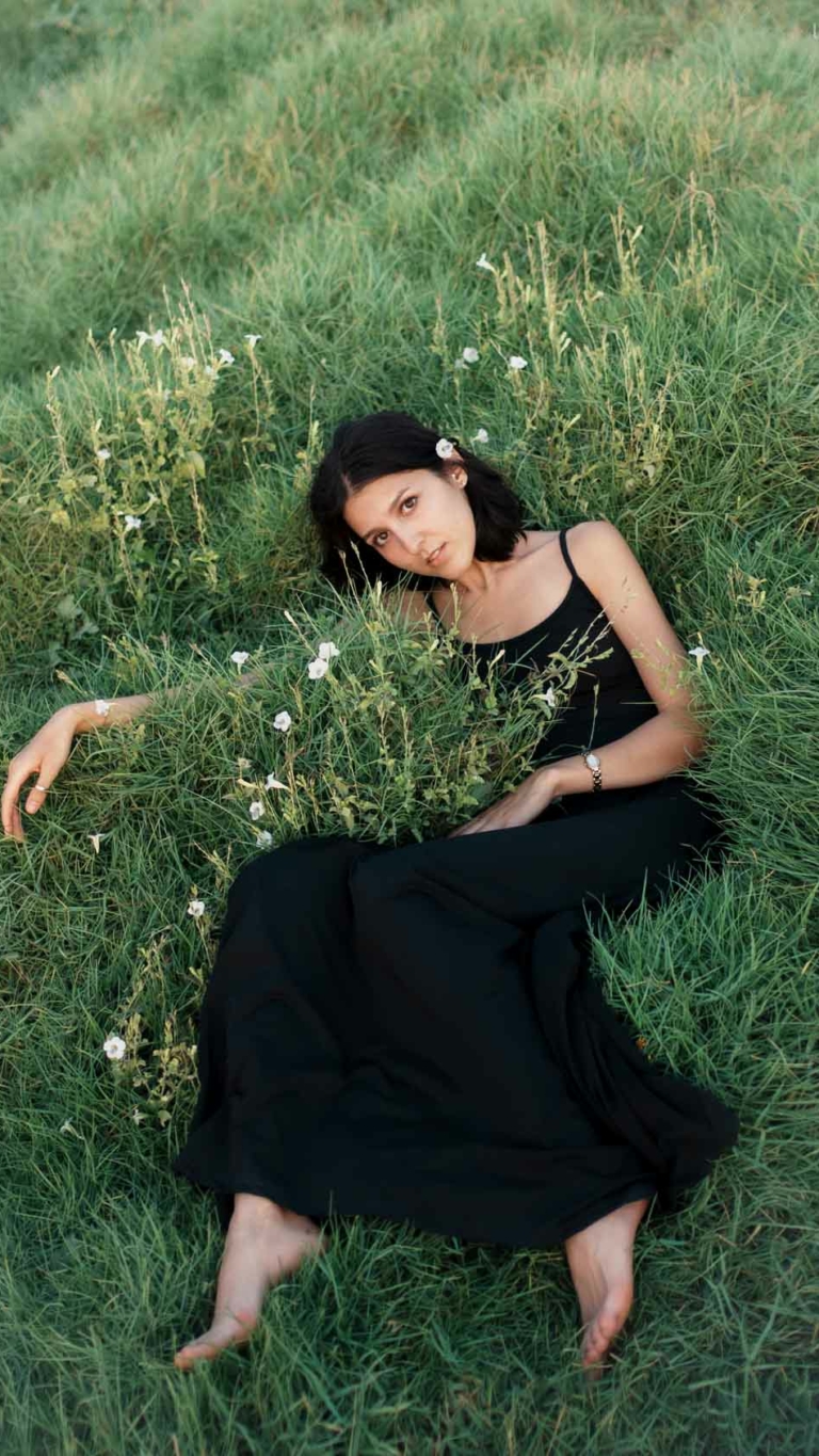 Woman in black dress amidst serene nature captured by Alisha Geva