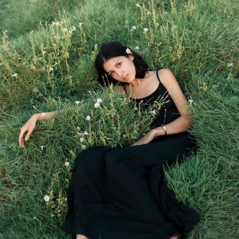Woman in black dress amidst serene nature captured by Alisha Geva