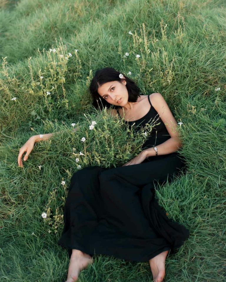 Woman in black dress amidst serene nature captured by Alisha Geva