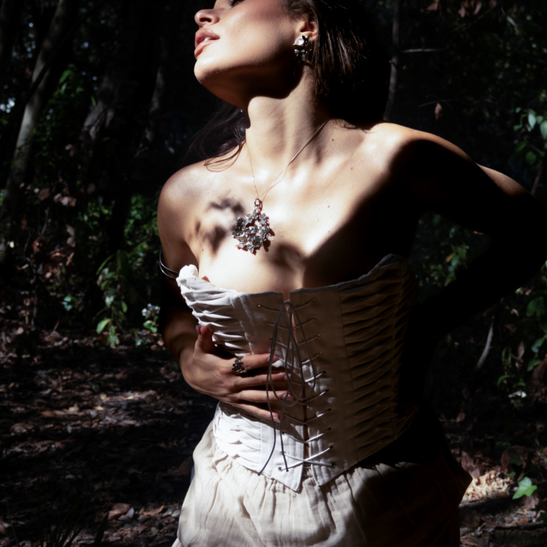 Portrait of a woman wearing a white corset and sculptural pendant, lit by dramatic shadows outdoors