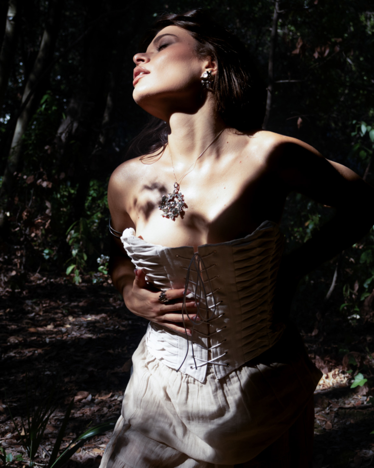 Portrait of a woman wearing a white corset and sculptural pendant, lit by dramatic shadows outdoors