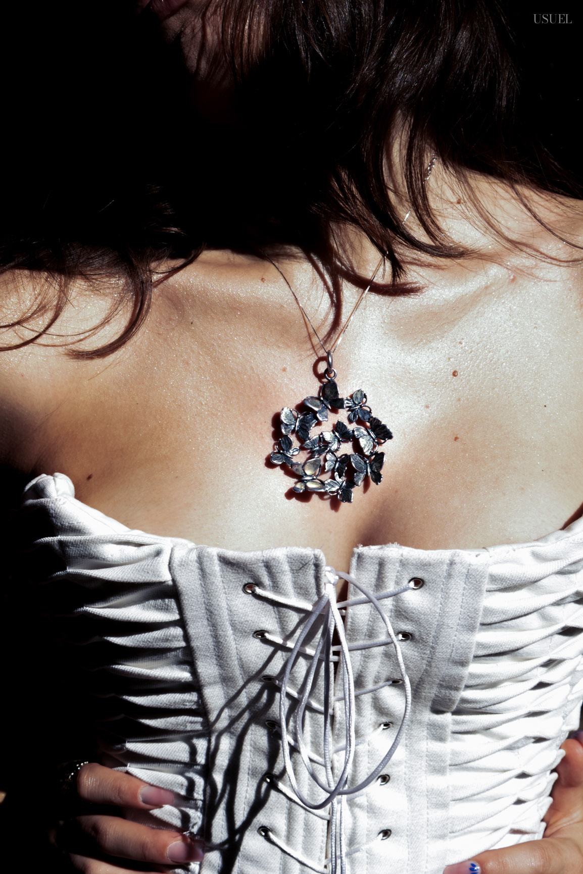 Close-up of a sculptural silver butterfly-like pendant necklace worn over a laced white corset