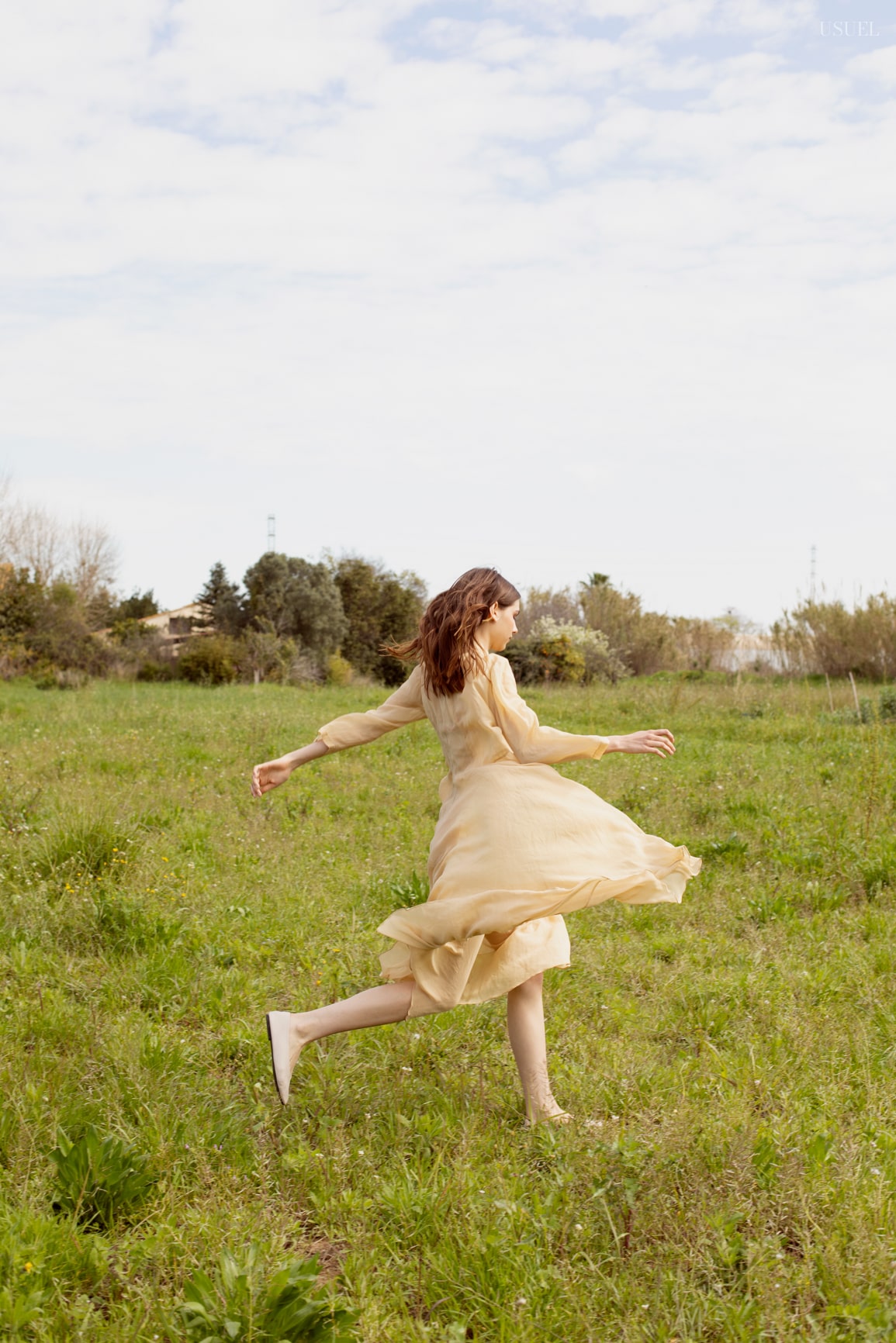 Model Lina wearing light, flowing garments made of tulle and lace, standing in the grass.