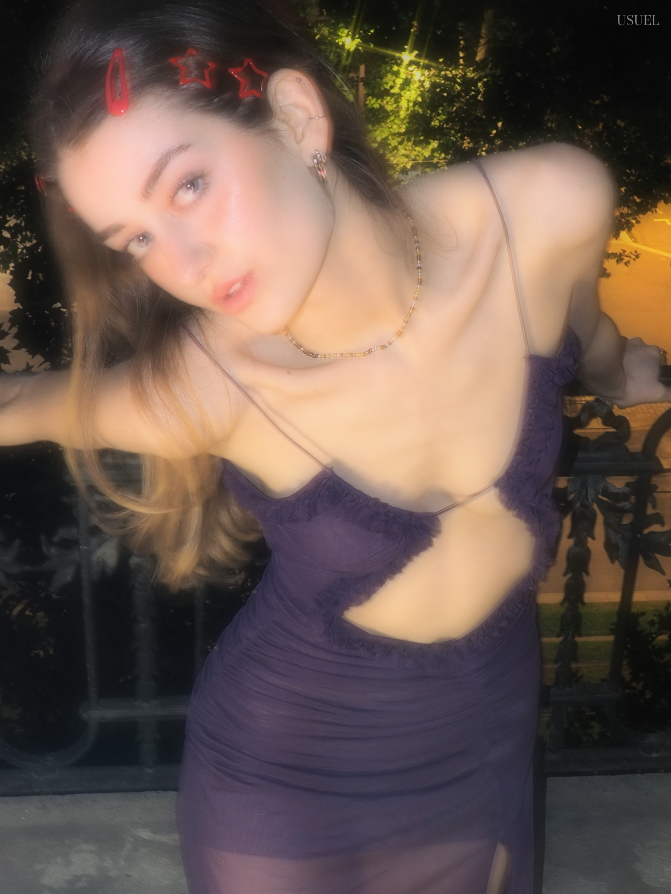Woman in a purple dress posing near a window at night