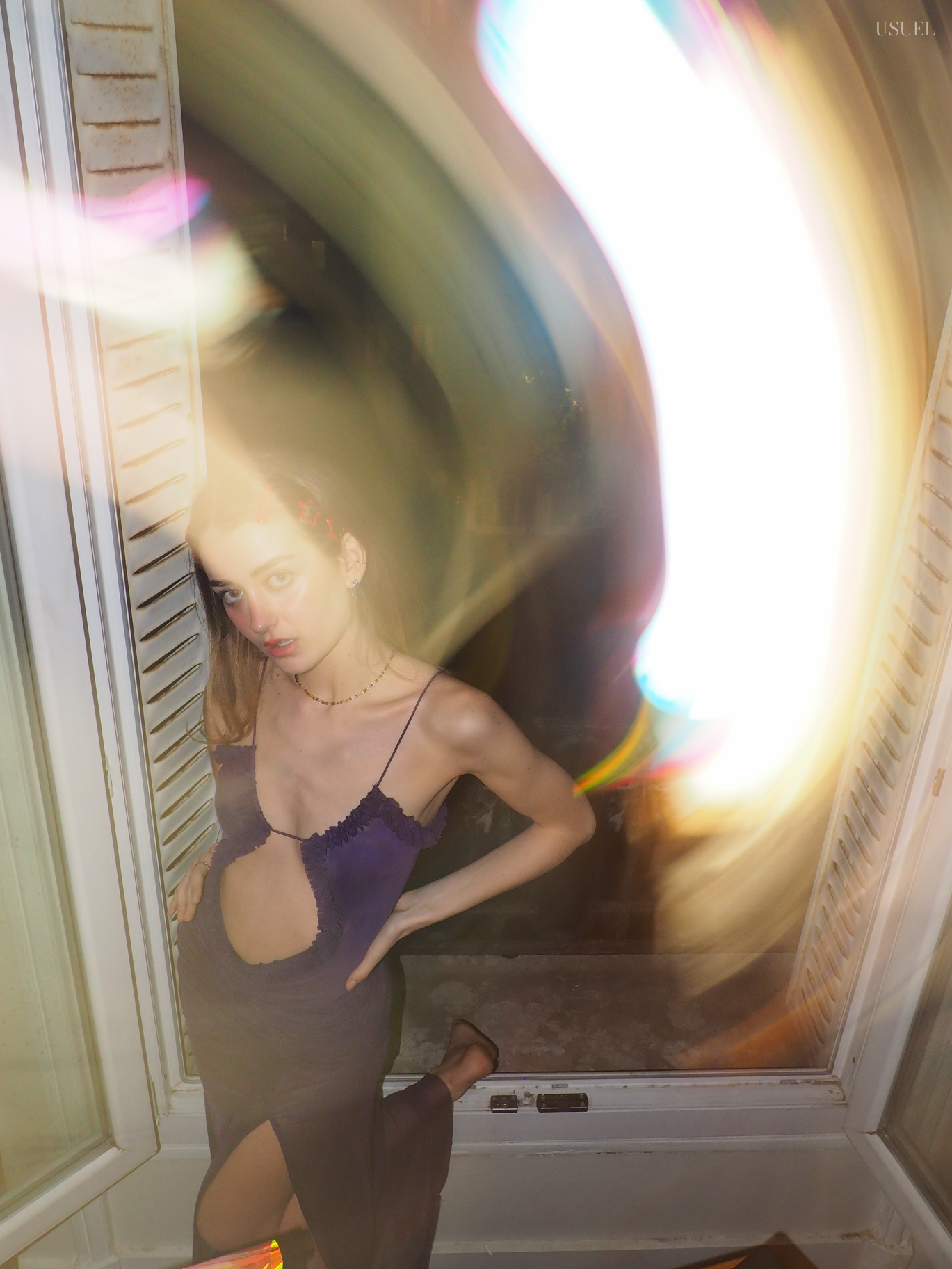 Woman in a purple dress posing near a window at night