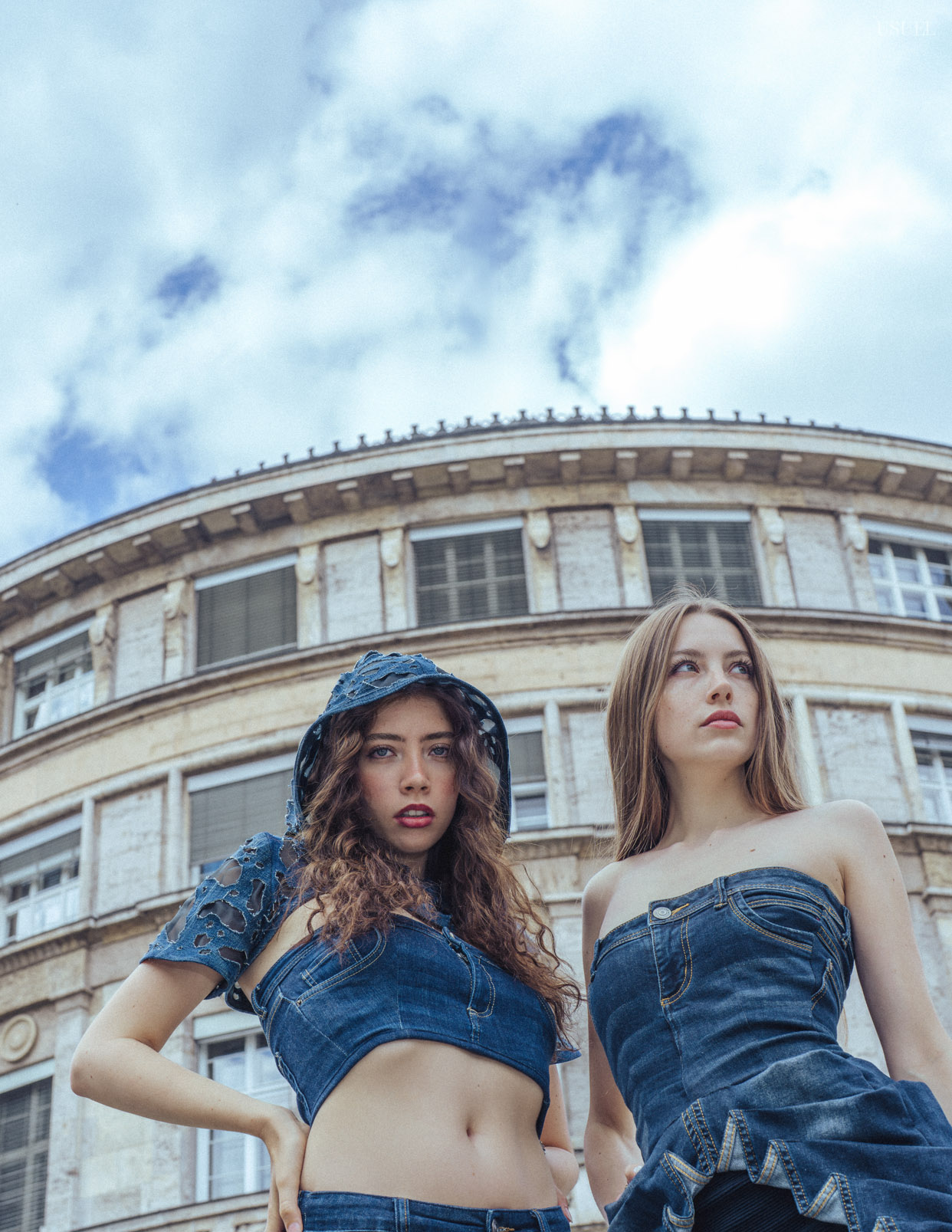 Two women wearing denim outfits, standing close to each other in an expressive pose